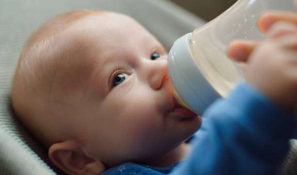 Baby boy sucks a bottle of milk, bottle warmer