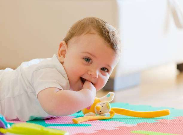 The baby is sitting on the bed with the bottle warmer on.