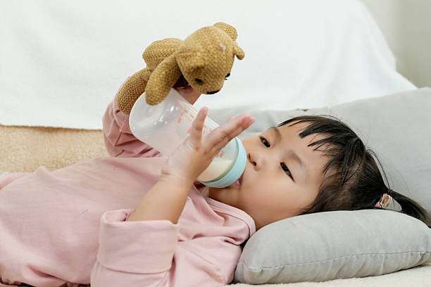 Young daughter lying on sofa drinking milk.bottle warmer