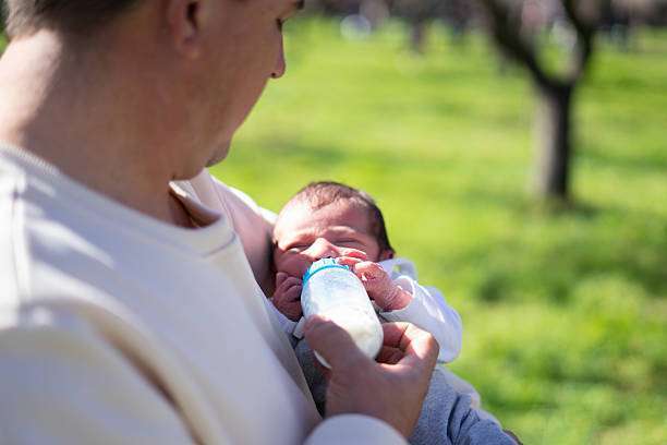 Grandfather holding and feeding his newborn grandson with a milk bottle in a park. bottle warmer