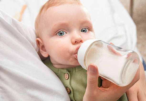 baby in mother's arms drinks from a bottle warmer