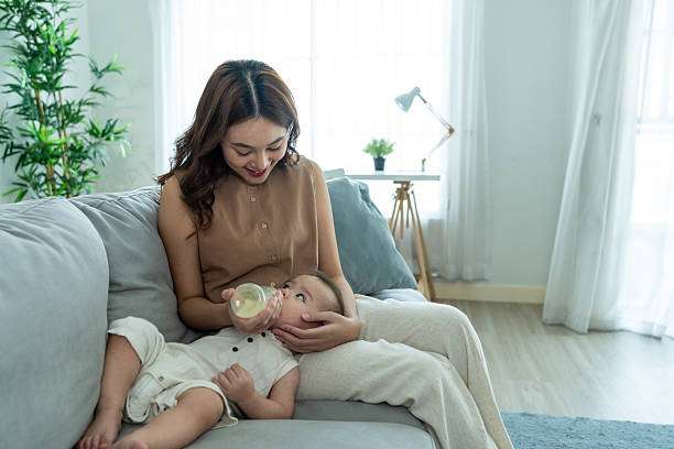 Asian beautiful mother holding and feeding baby from milk bottle. bottle warmer